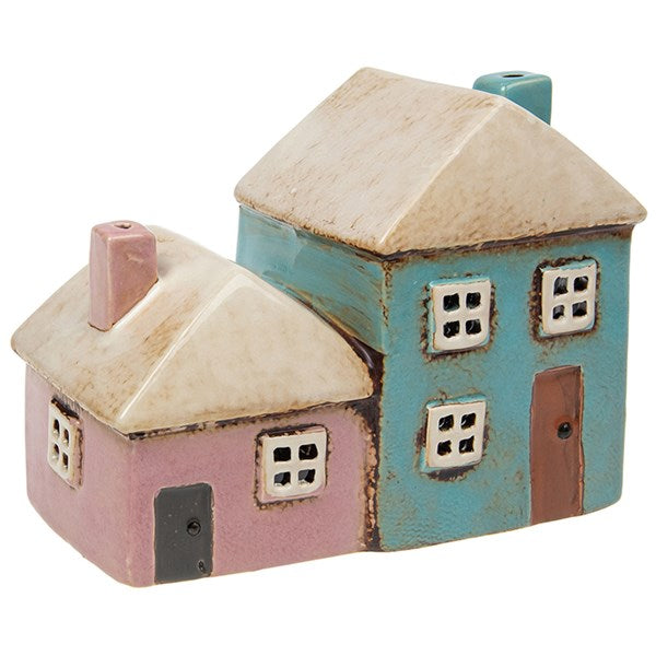 Add a whimsical glow to your sacred space with our Village Pottery Pink & Aqua Two Houses Tealight Holder. Lovingly handcrafted, this ceramic tealight features two quaint cottages in soft pastel pink and aqua, complete with rustic windows and textured detailing.
Perfect for your altar, windowsill, or cozy corner, it casts a warm, inviting light through its cut-out windows—creating an enchanting atmosphere in any room. A magical décor piece for lovers of folklore, cottagecore, or handmade British potter