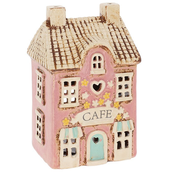 In the heart of the enchanted village, there is a little café where whispers of magic mingle with the scent of freshly brewed tea. This charming Village Pottery Café Tealight Holder by Shudehill Village Pottery captures that very spirit. Crafted with care and rich in rustic detail, it measures 15.5 x 9.5 x 8cm — the perfect size to nestle upon your altar, windowsill, or cosy reading nook. When you place a tealight within, warm light flickers through its tiny windows, casting spellbound shadows across the ro