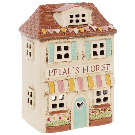 Handcrafted in the Village Pottery workshop, this  Florist tealight holder is a true collectors item from the Shudehill collection. Made in ceramic with intricate detailing, it beautifully captures the nostalgic charm of a festive florist shop in a winter village scene. Measuring 16 x 10.5 x 7.8cm, it glows warmly when lit with a tealight, filling your home with cosy seasonal atmosphere. Perfect for mantelpieces, shelves, or as part of a Christmas village display, this piece is both decorative and coll