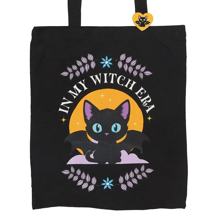 Step out in spooky style with this polycotton tote bag featuring the phrase ‘In My Witch Era’ alongside an enchanting bat-winged black cat. Complete with a matching enamel pin, it’s the perfect everyday accessory for those who love all things mystical.