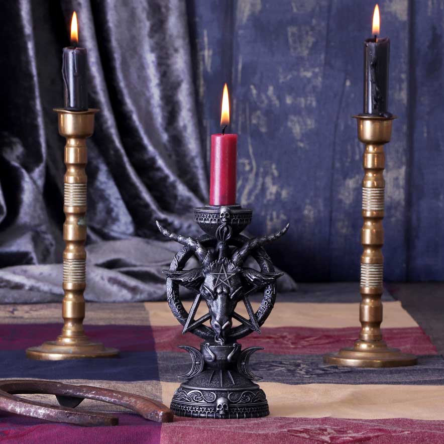 Decorative candle holder with a red candle flanked by two brass candlesticks on a dark fabric background.