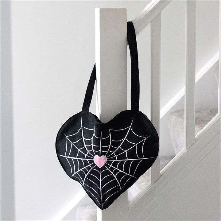 Heart-shaped black bag with spider web design and pink heart on a white staircase.