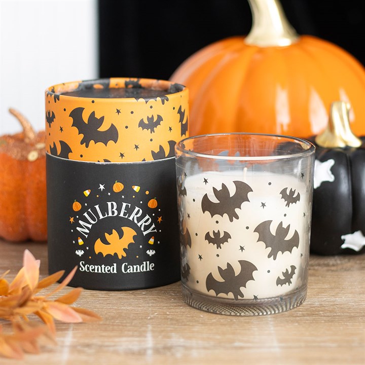 Halloween-themed scented candle with bat design and pumpkins in the background