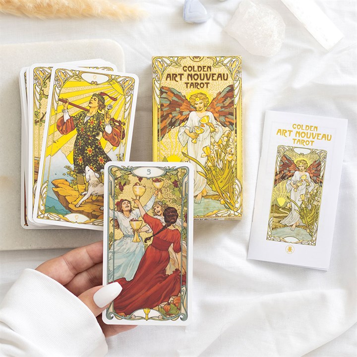 Golden Art Nouveau Tarot cards with a hand holding one card on a white surface