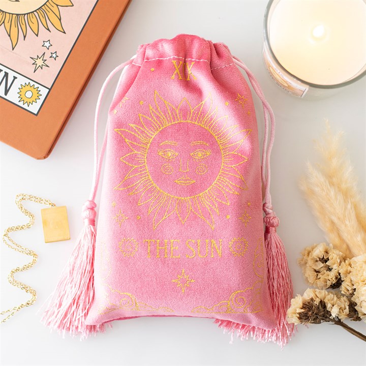 Pink drawstring bag with sun design and 'The Sun' text on a white surface with tarot cards and candle.