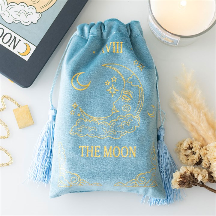 Blue drawstring bag with gold moon design and 'The Moon' text on a white surface with tarot cards and candles.