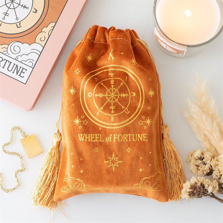 Orange drawstring bag with 'Wheel of Fortune' design on a light surface with a candle and card in the background.