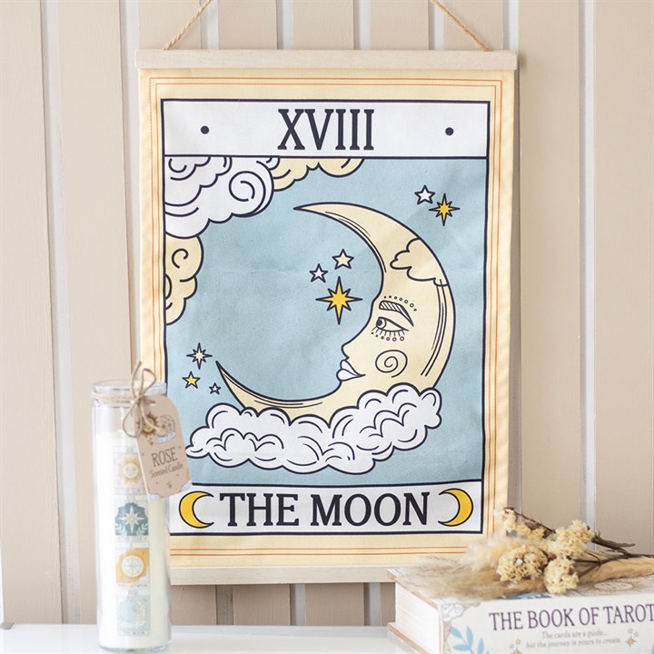 Framed tarot card titled 'The Moon' with a candle and book on a table.