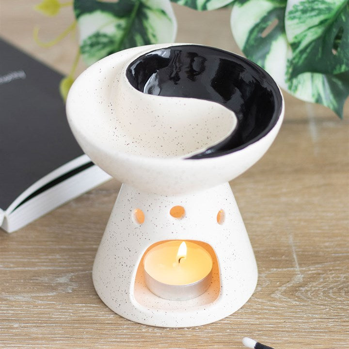 Ceramic oil burner with a lit candle on a wooden surface