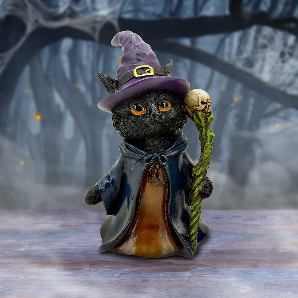 Cat figurine in a witch costume with a purple hat and staff, standing on a wooden surface with a dark background.