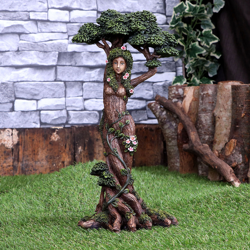 Statue of a woman intertwined with tree branches and foliage against a stone wall background.