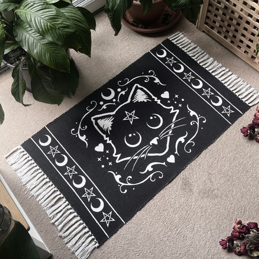 Welcome a familiar spirit into your home.
As any witch worth their potions knows, no hearth or altar is complete without the protective presence of a magical black cat. Now, you can honour your mystical companion with this beautifully handcrafted Alchemy Gothic ‘Purrfect’ Cat Rug.
Featuring an original black cat and magical symbol design from Alchemy, this tasseled, hand-woven rug adds an enchanting touch to any sacred space—whether placed by the fireplace, on the wall, or beneath your spellwork on the alt