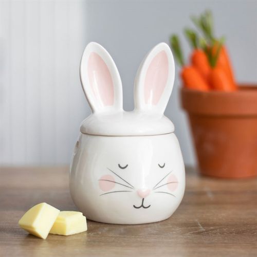 Ceramic jar shaped like a rabbit with a lid on a wooden surface, next to carrots and butter.