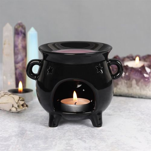 Black ceramic oil burner with a lit candle inside, surrounded by candles and crystals on a gray surface.
