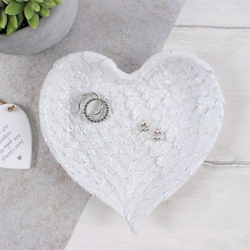 Heart-shaped white ceramic dish with jewelry on a light wooden surface