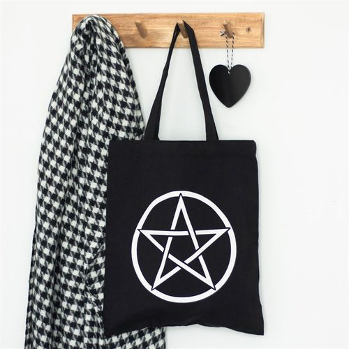 Black tote bag with a white pentagram design, houndstooth scarf, and black heart-shaped object on a wooden hook against a white wall.