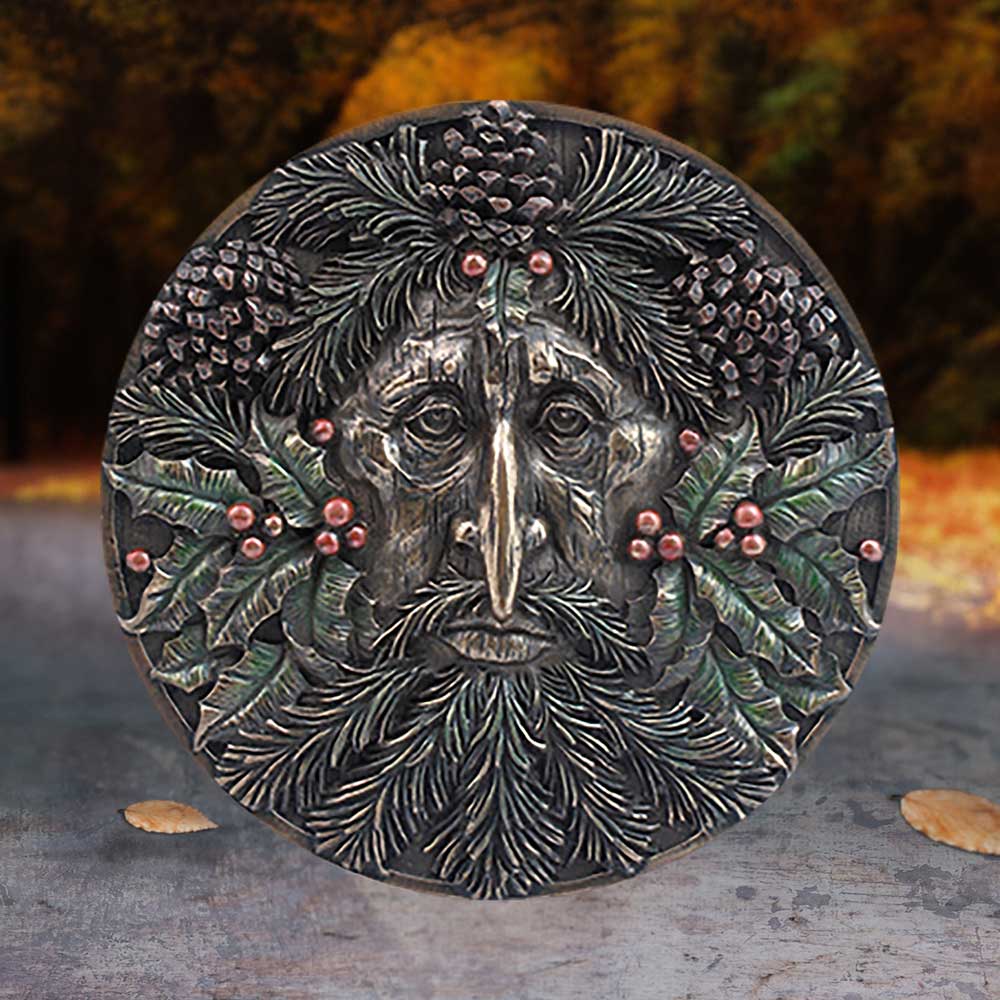 Decorative plaque with a face surrounded by leaves and berries on a textured surface.
