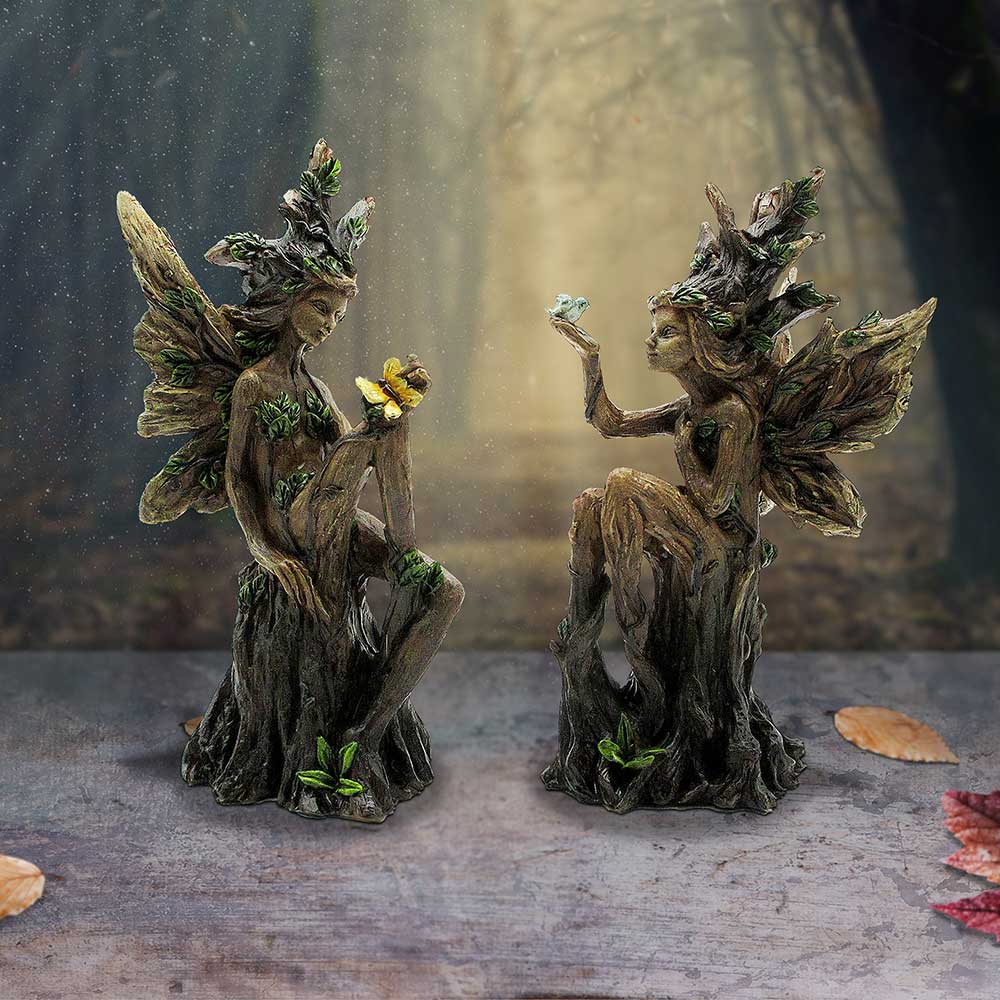 Two fairy figurines with leafy wings on a wooden surface with a forest background.