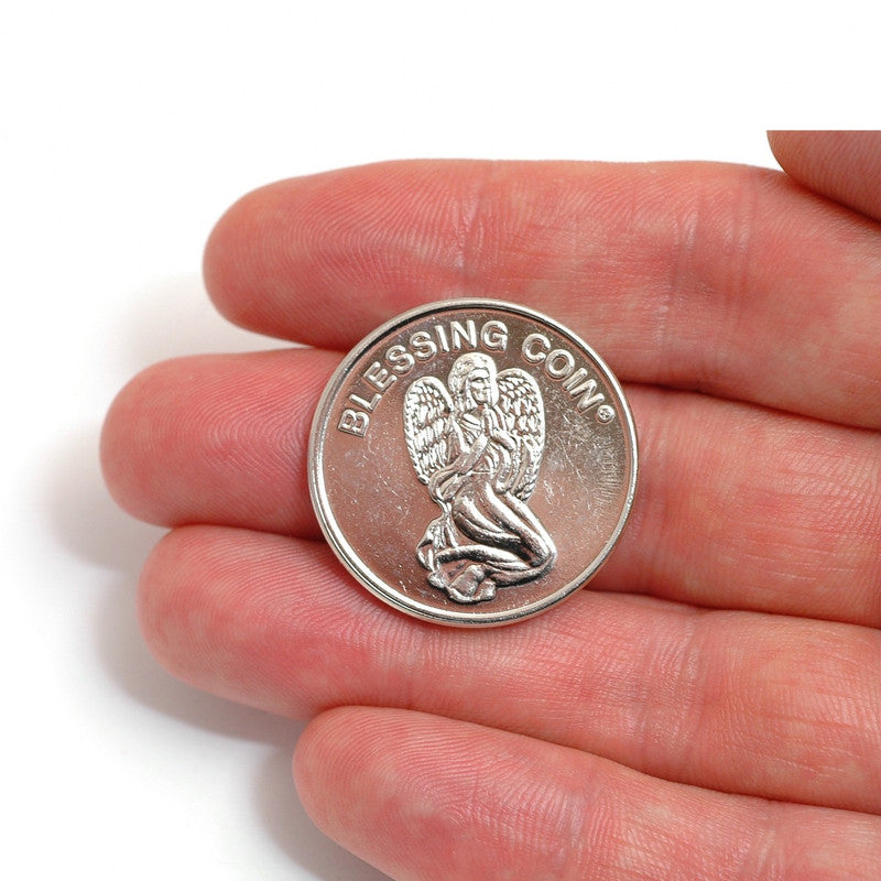 Silver coin with angel design held in a hand on a white background
