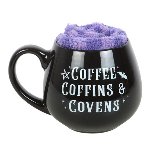 Get cosy in true witchy style with the Coffee, Coffins & Covens Cauldron Mug & Fluffy Socks Gift Set — the perfect pairing for spell-casting Sundays, moonlit movie marathons, and lazy mornings with your favourite brew.

This enchanting set features a 450ml cauldron-shaped ceramic mug emblazoned with the gothic phrase “Coffee, Coffins & Covens”, celebrating caffeine, comfort, and a touch of the macabre. Paired with a pair of soft purple fluffy socks, it brings together warmth and wicked charm for the ultimat