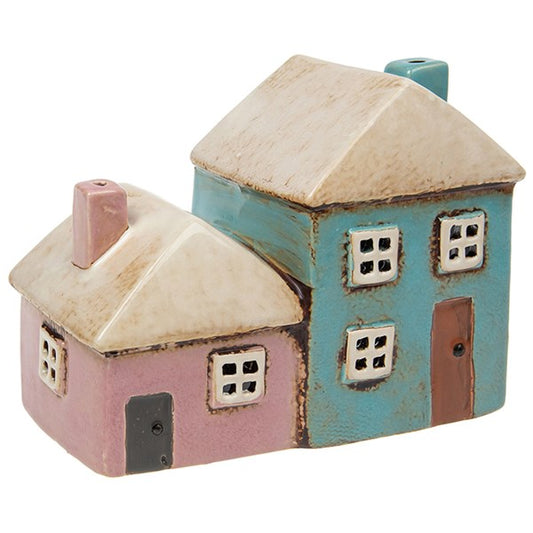 Add a whimsical glow to your sacred space with our Village Pottery Pink &amp; Aqua Two Houses Tealight Holder. Lovingly handcrafted, this ceramic tealight features two quaint cottages in soft pastel pink and aqua, complete with rustic windows and textured detailing.

Perfect for your altar, windowsill, or cozy corner, it casts a warm, inviting light through its cut-out windows—creating an enchanting atmosphere in any room. A magical décor piece for lovers of folklore, cottagecore, or handmade British potter