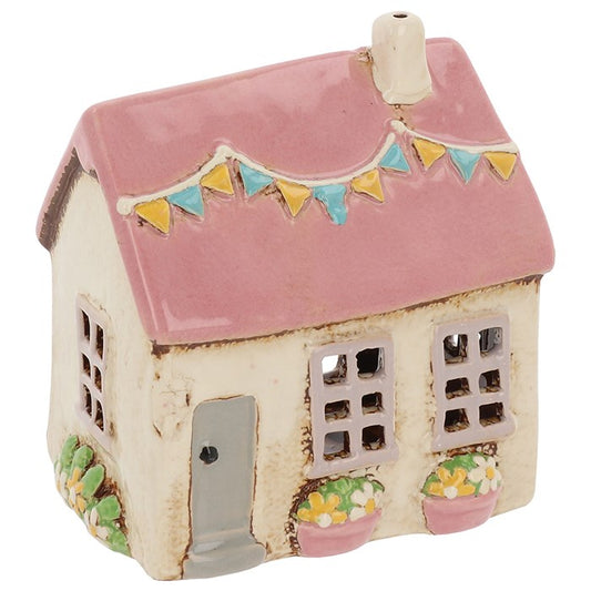 In the quiet heart of the village, where moonlight kisses the cobblestones, stands this charming pottery house — a keeper of gentle light and whispered magic. Crafted in a warm cream glaze, its walls are adorned with tiny raised flags, a symbol of gatherings, merriment, and blessings on the wind. When a tealight glows within, soft golden light spills through its windows, casting dancing shadows that seem to tell stories of old. Perfect for a witch’s garden altar, a cozy hearth nook, or as a welcoming beacon