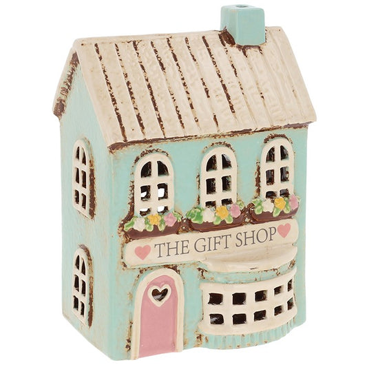 Beyond the cobbled path lies the heart of the village — the gift shop where trinkets, charms, and treasures wait to be discovered. This Village Pottery Gift Shop Tealight House, measuring 17.5 x 12 x 9cm, captures that very magic in ceramic form. By day, its hand-painted details tell the tale of a bustling village shop; by night, a tealight placed inside awakens it, sending warm golden light spilling from its tiny windows. Ideal for witches who weave enchantment into their home, it’s a keepsake that glows w