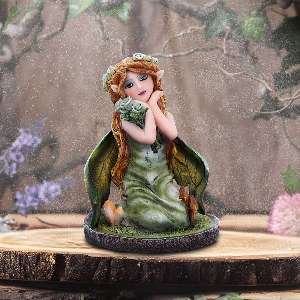 Fairy figurine with green dress and flower crown on a wooden platform with nature-themed background