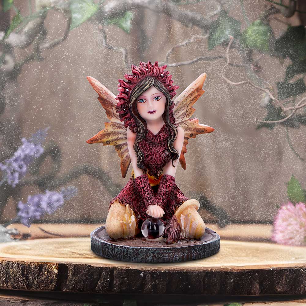 Fairy figurine with wings and a crystal ball on a wooden base with a nature-themed background.