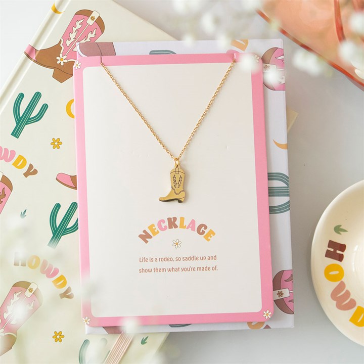 Gold necklace with a cowboy boot pendant on a decorative card with cactus designs.