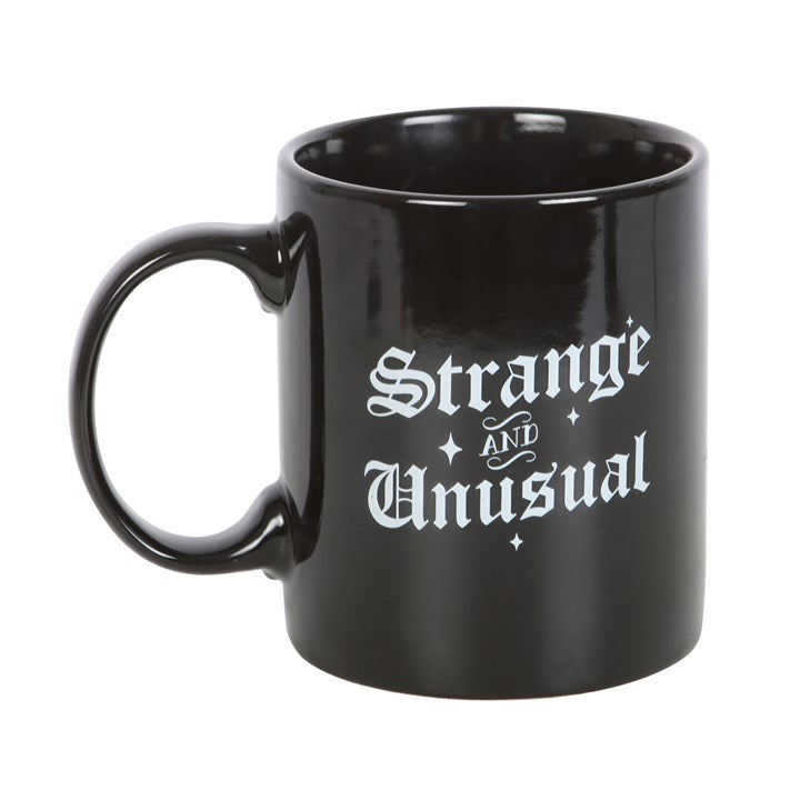 Summon a smile with every sip and embrace your shadowy charm with the Strange and Unusual Mug. Crafted from smooth ceramic and finished with bold gothic lettering, this delightfully peculiar mug proudly declares your love for the weird, the wonderful, and the delightfully dark.

With the phrase “Strange and Unusual” emblazoned across its front, this mug is perfect for those who prefer moonlit mornings and coffee as black as their wardrobe. Its 300ml capacity makes it ideal for your daily dose of caffeine, t