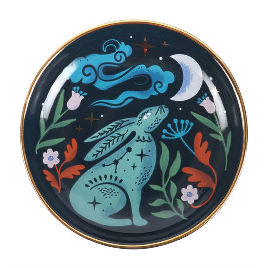 This enchanting Midnight Hare Trinket Dish captures the magic of a moonlit night with its exquisite ceramic design. Featuring a serene hare gazing up at a star-studded sky, the dish is adorned with delicate golden accents that shimmer like hidden spells. Its rounded shape offers a perfect sanctuary for your cherished trinkets, rings, and jewellery, keeping them safe while adding a touch of mystical charm to your altar or dressing table. Embrace the quiet power of the night and let this dish hold your treasu