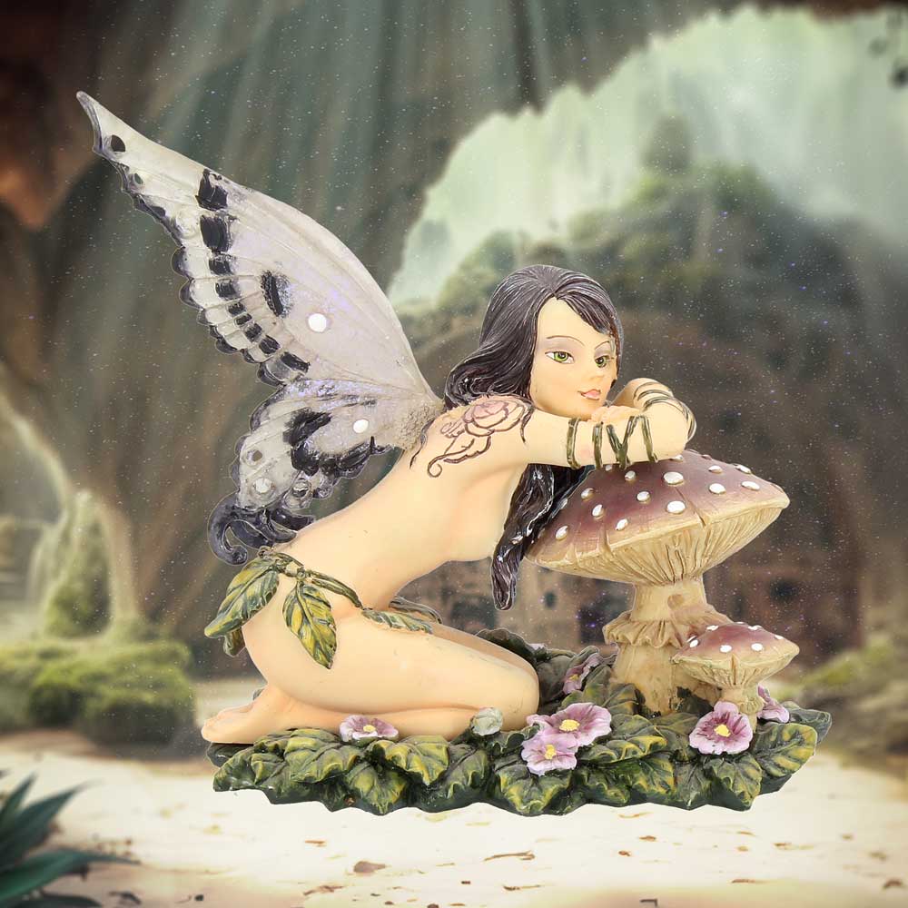 Fairy figurine with butterfly wings sitting on a mushroom in a fantasy forest setting