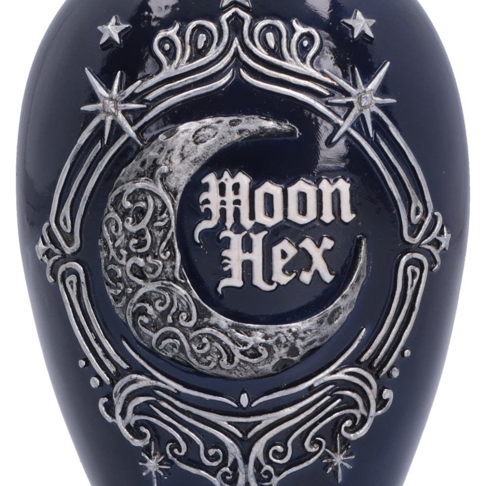 Close-up of a glossy dark navy blue bottle or container featuring a raised silver crescent moon, stars, ornate scrollwork, and the words 'Moon Hex' in white gothic lettering.