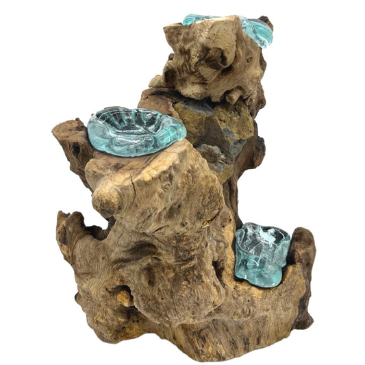 Bring soulful light into your home with our Molten Glass Triple Candle Holder on Wood. Handcrafted in Bali from recycled molten glass and natural Gamal wood, each piece is a unique union of earth and fire. The molten glass is shaped while hot and naturally fused to the contours of the wood, creating three organic bowls for tealights or candles.