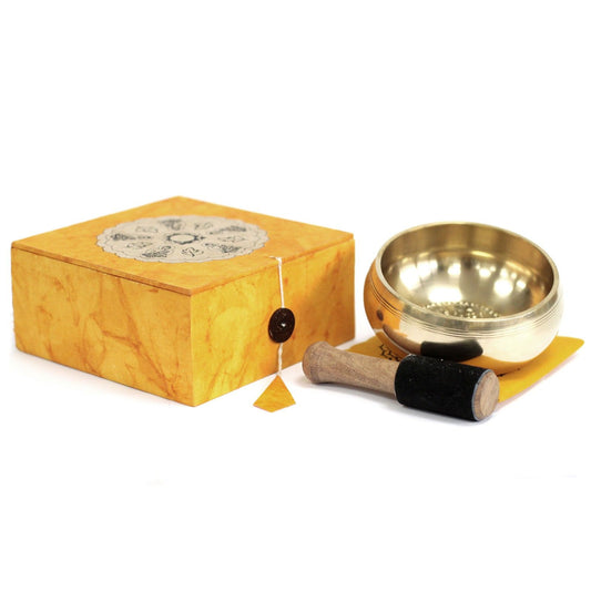 Brass singing bowl with wooden striker and yellow box on a white background