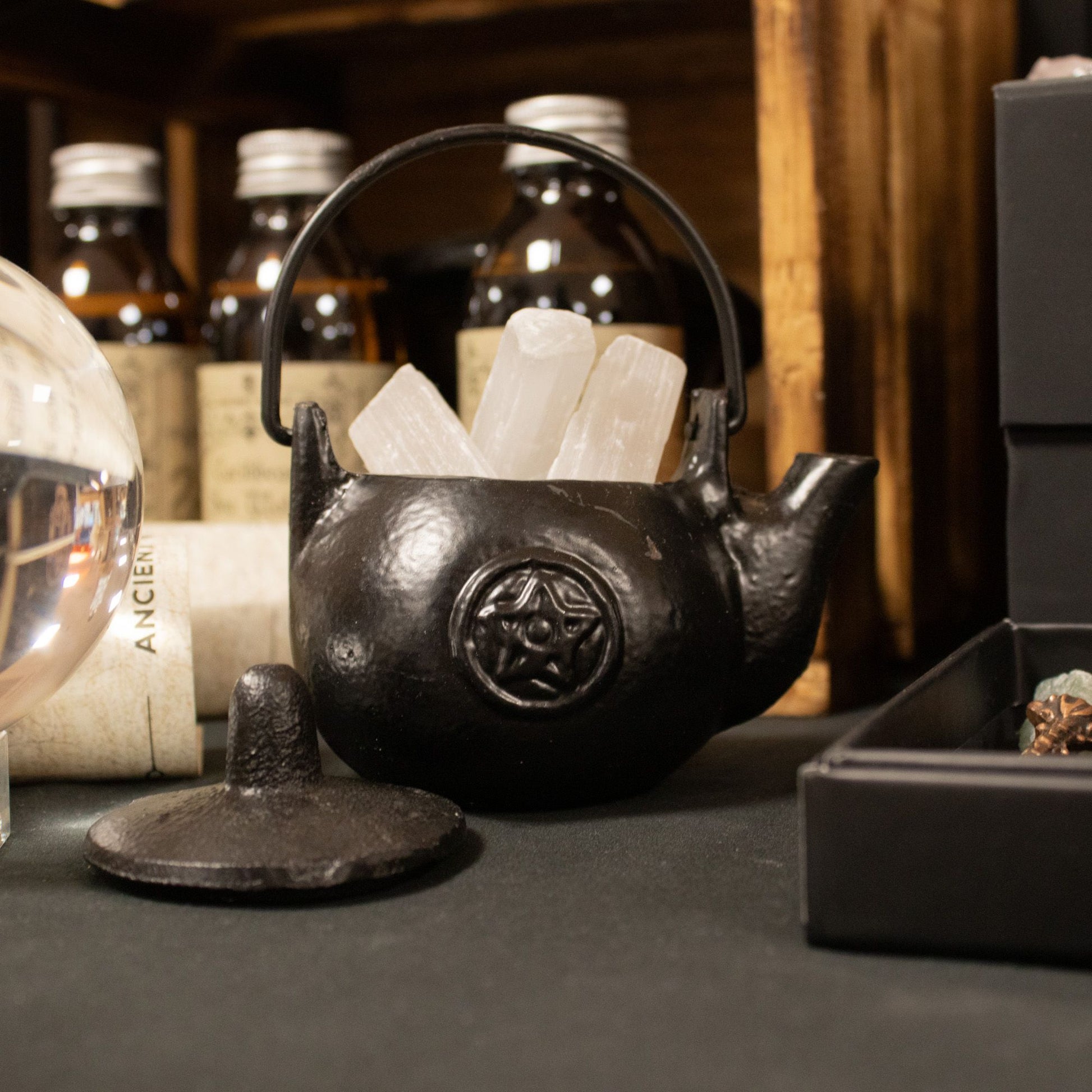 A darkly elegant ritual pot forged from solid cast iron, crowned with a protective lid and commanding side handle. The pentagram embossed upon its surface marks it as a vessel for serious craft—perfect for burning sacred herbs, charcoal, or incense during your most potent workings. Compact yet commanding, this 8x8x10cm cauldron sits perfectly on altar or shelf, radiating gothic presence. The cast iron construction holds heat steadily, containing ash and smoke between rituals while its fitted lid keeps your 