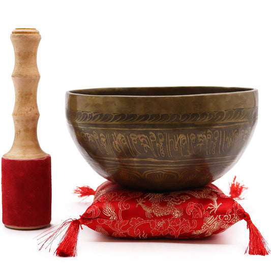 Bronze singing bowl with decorative patterns on a red cushion, accompanied by a wooden mallet.