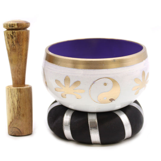 White singing bowl with gold designs, purple interior, and wooden striker on a white background