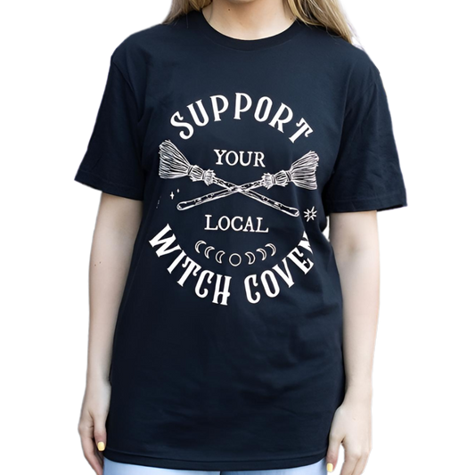 Show your support for the sisterhood with this unisex ‘Support Your Local Witch Coven’ T-shirt, crafted for witches, mystics, and seekers of the old ways.

This classic black cotton tee carries a powerful message: “Support Your Local Witch Coven,” adorned with a broomstick and moon phases – sacred symbols of unity, cycles, and magic. In witchcraft, the coven is not just a gathering, but a circle of shared strength, wisdom, and protection. Wearing this shirt honors that ancient bond, a sign that you stand wi