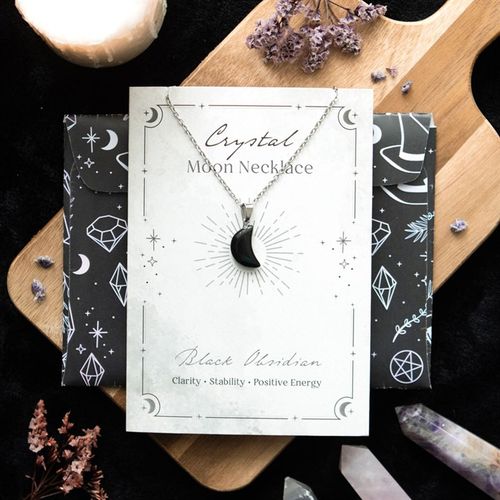 Crystal moon necklace on a branded card with decorative elements on a wooden surface.